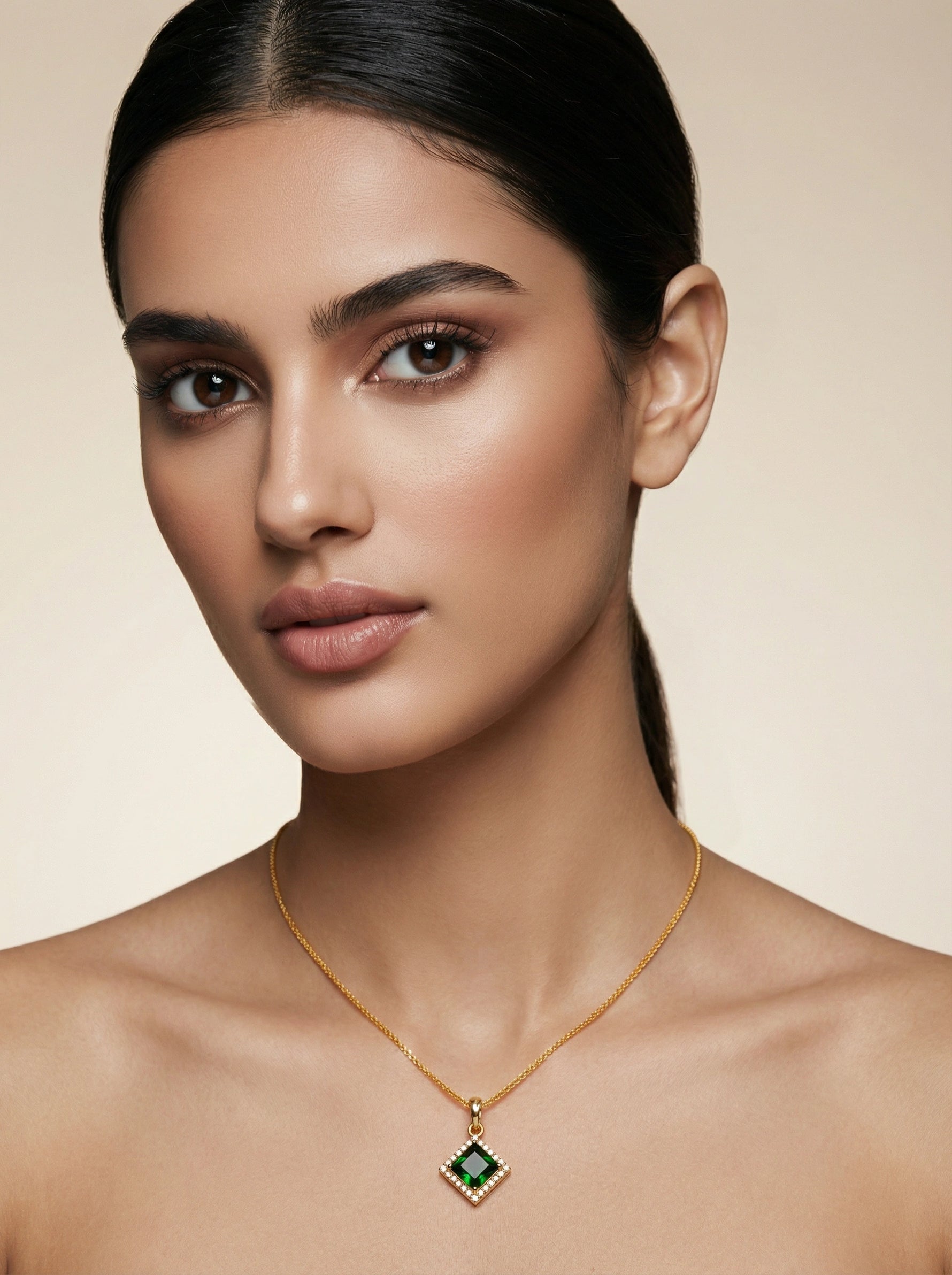 Woman wearing a 18k gold plated necklace with a green gemstone pendant against a beige background