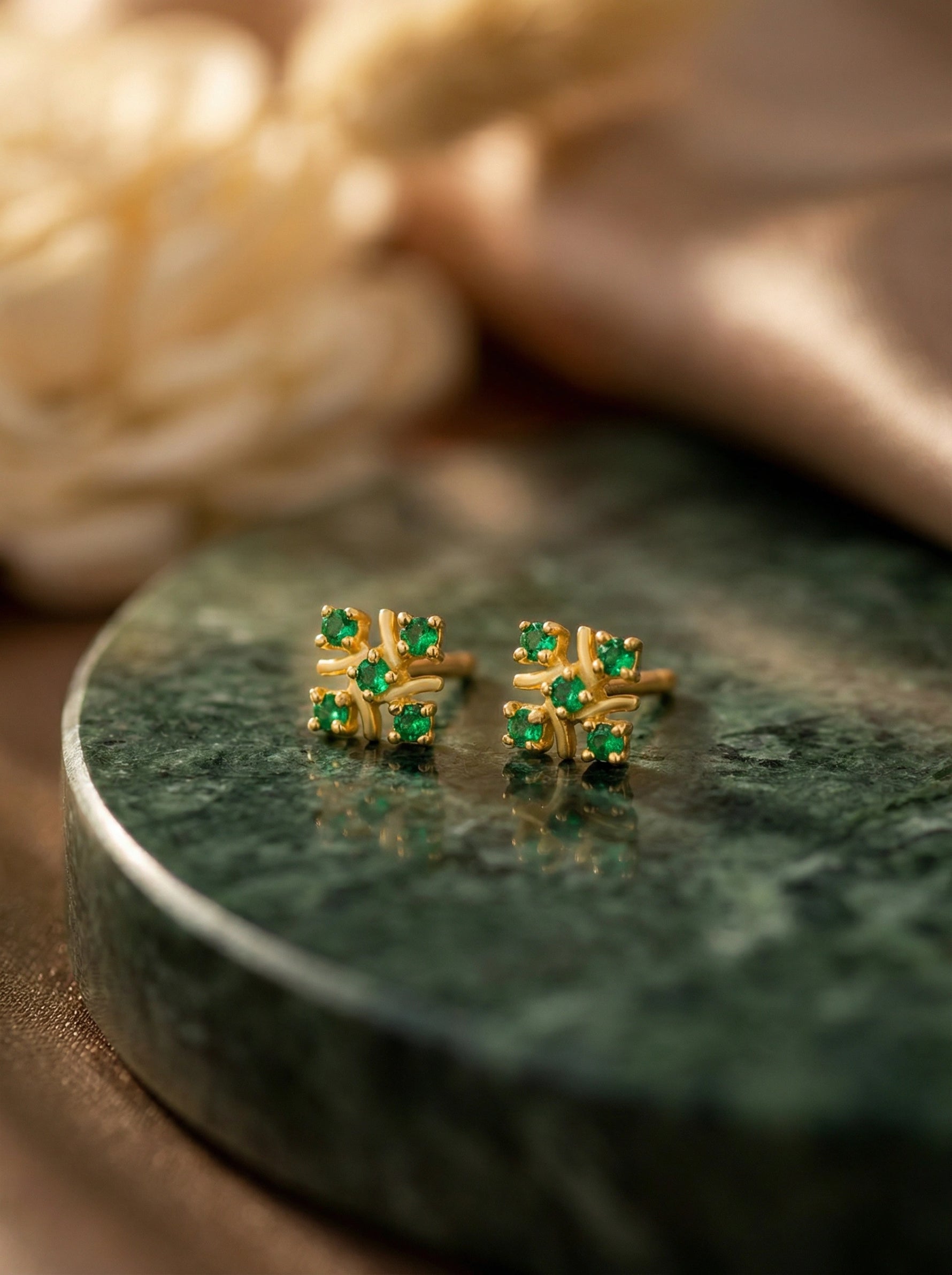 18k Gold plated earrings with green gemstones on a green marble surface