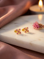 18k Gold plated earrings with pink stones on a marble surface with a candle in the background