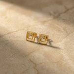 Pair of 18k  gold plated square earrings with embedded diamonds on a beige marble surface