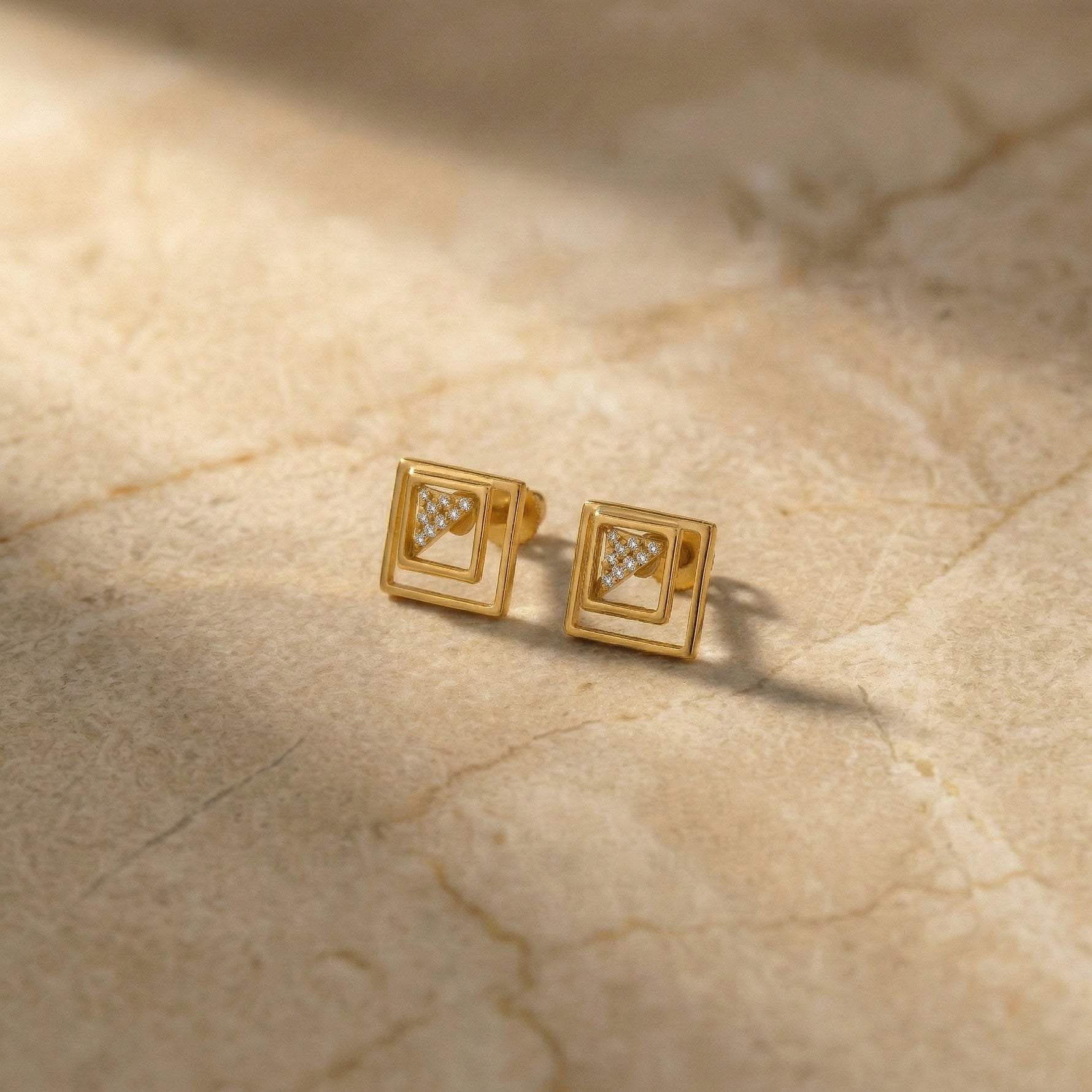 Pair of 18k  gold plated square earrings with embedded diamonds on a beige marble surface