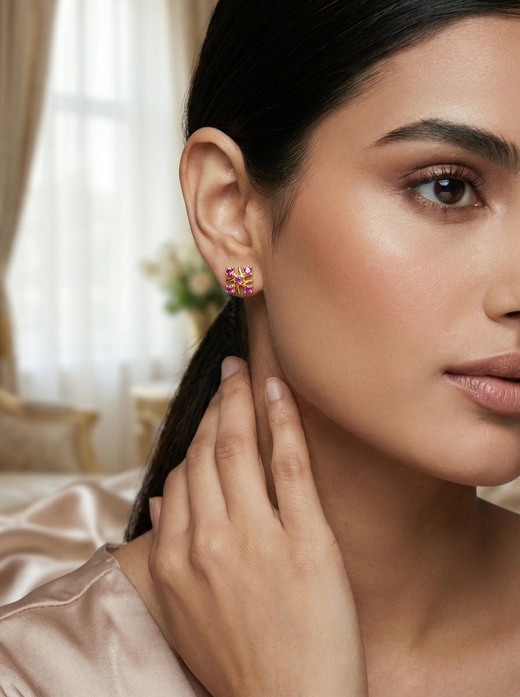 Close-up of a woman wearing 18k gold plated earrings with a blurred indoor background