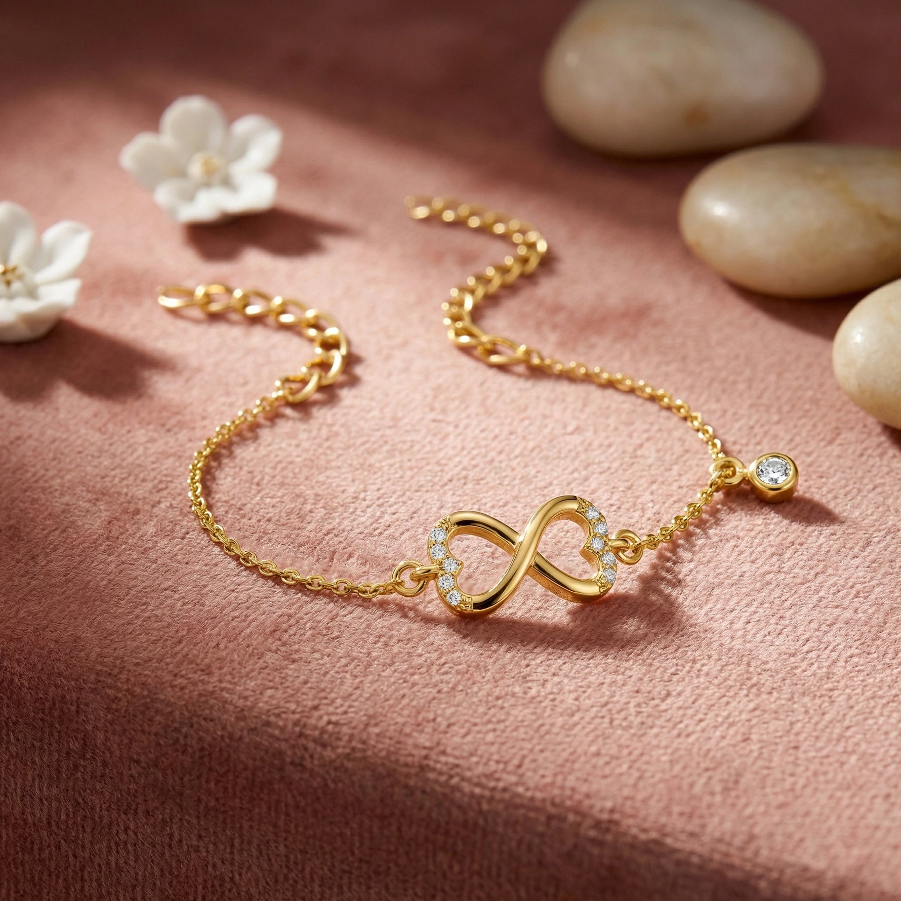 18k Gold plated bracelet with an infinity symbol on a pink surface with flowers and stones.