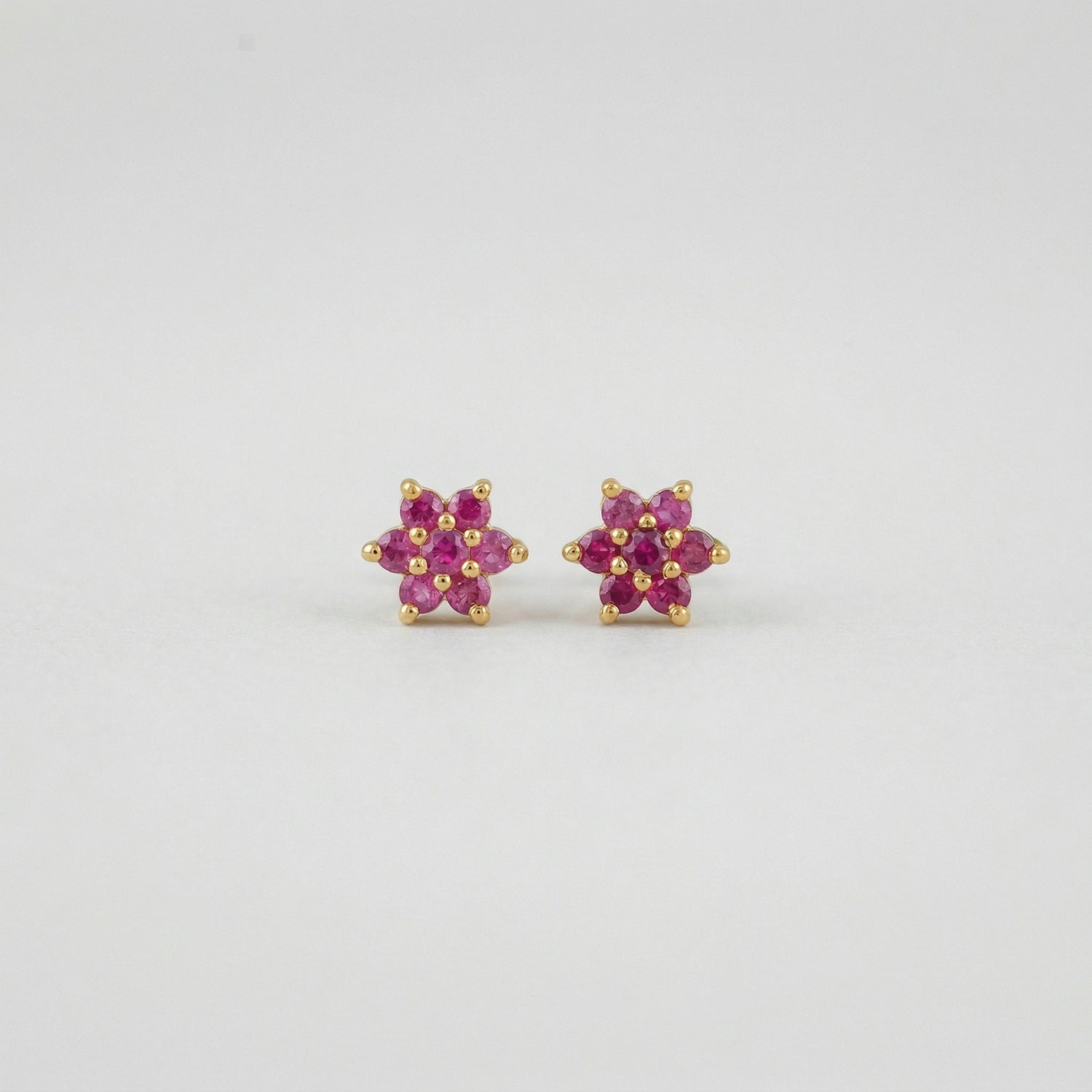 Pair of flower-shaped 18k gold plated  earrings with pink stones on a light gray background