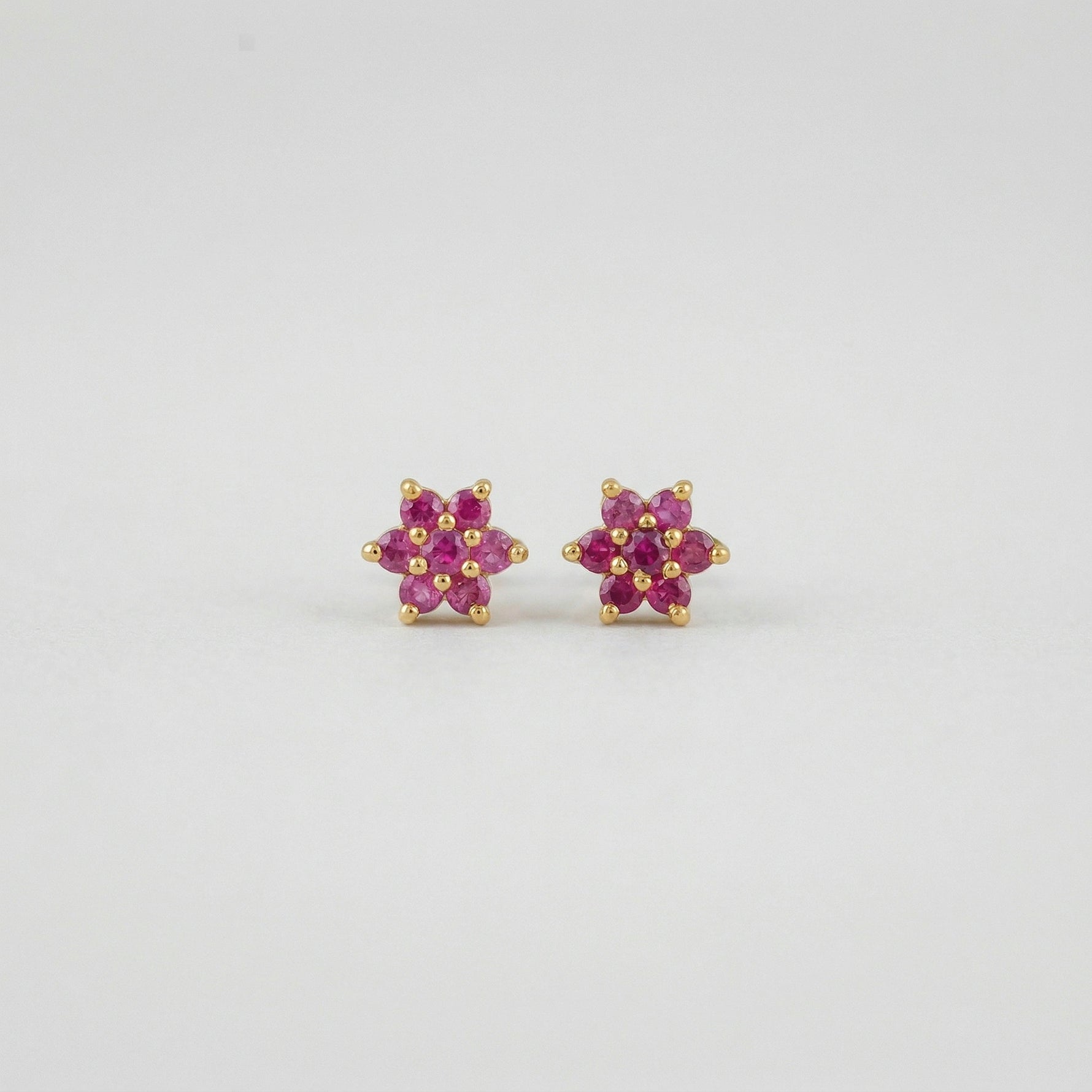Pair of flower-shaped 18k gold plated  earrings with pink stones on a light gray background