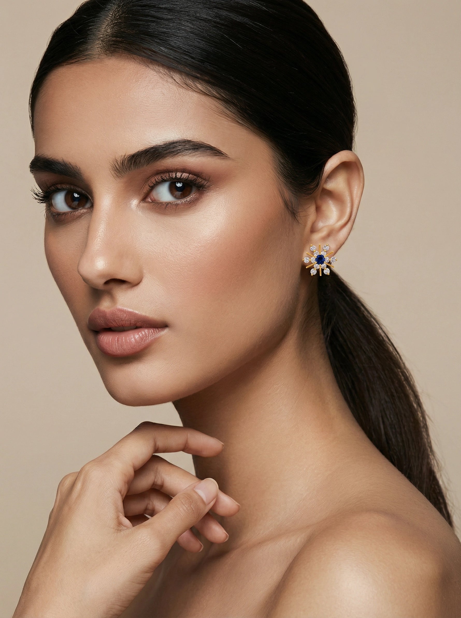 Woman wearing a blue gemstone with 18k gold plated earring against a beige background