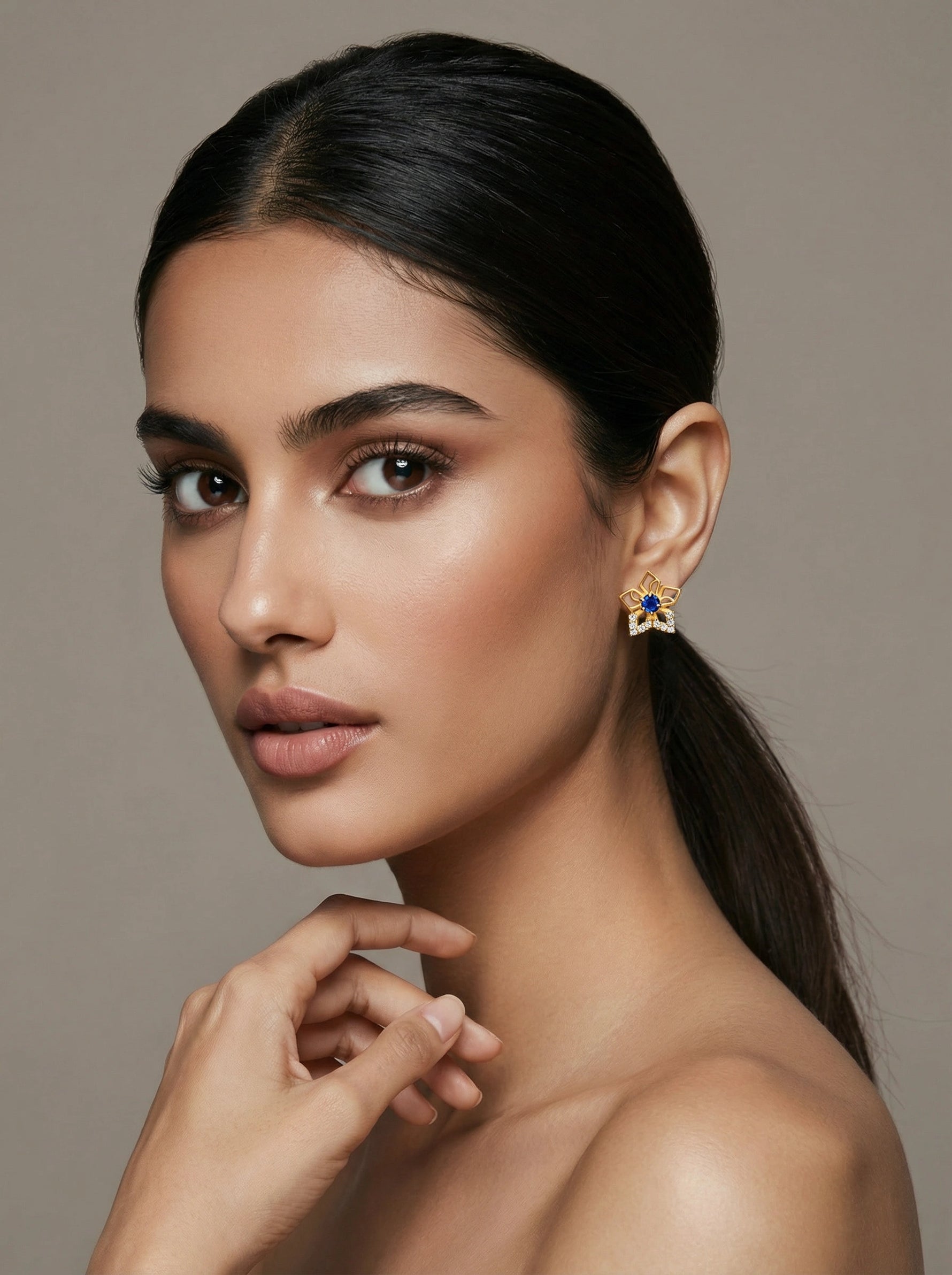 Woman wearing a 18k gold plated earring with a blue gemstone against a neutral background