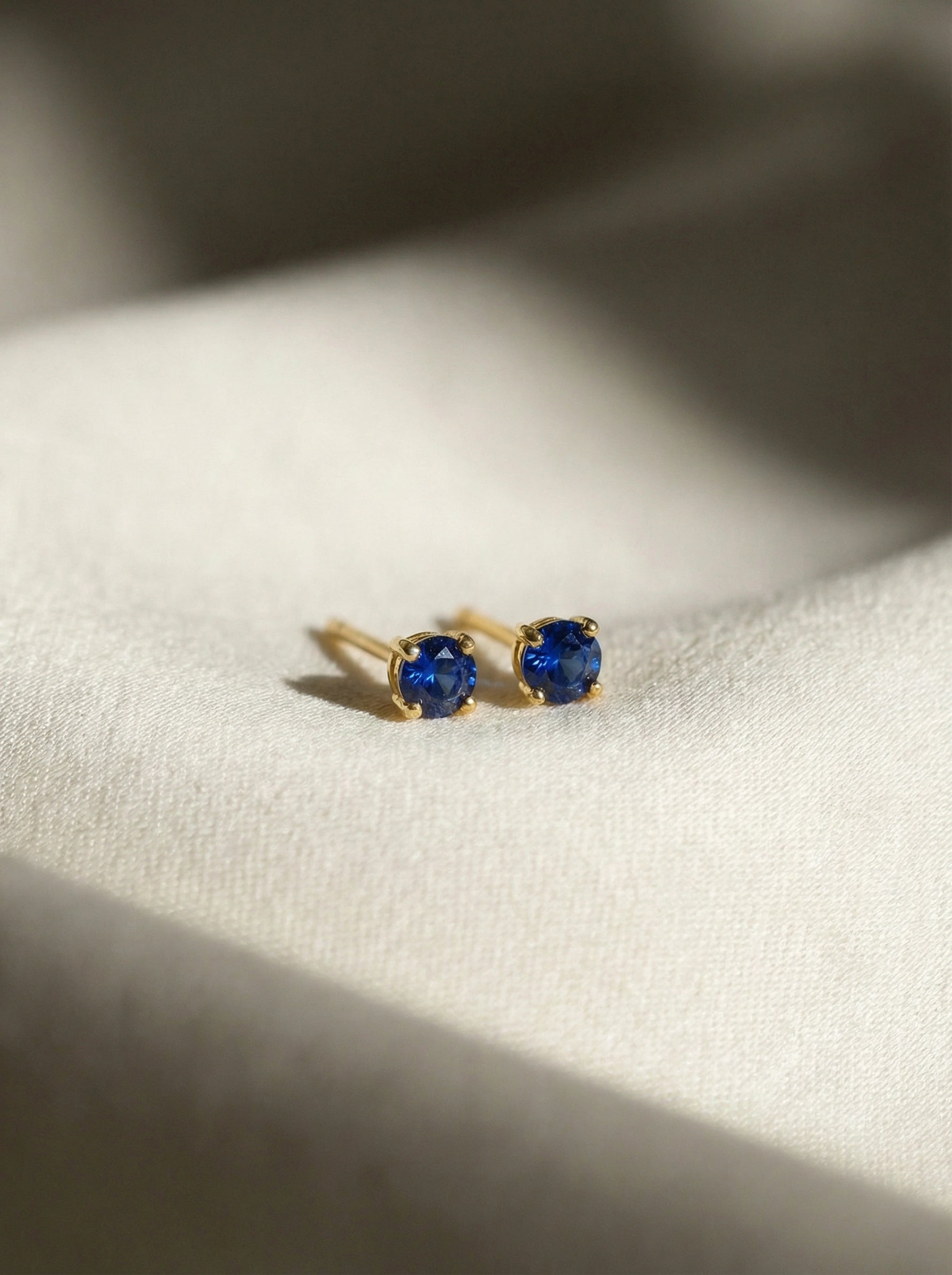 18k Gold plated earrings with blue gemstones on a white fabric background