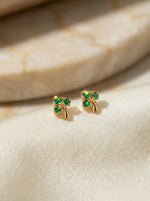 18k Gold plated earrings with green gemstones on a beige fabric background