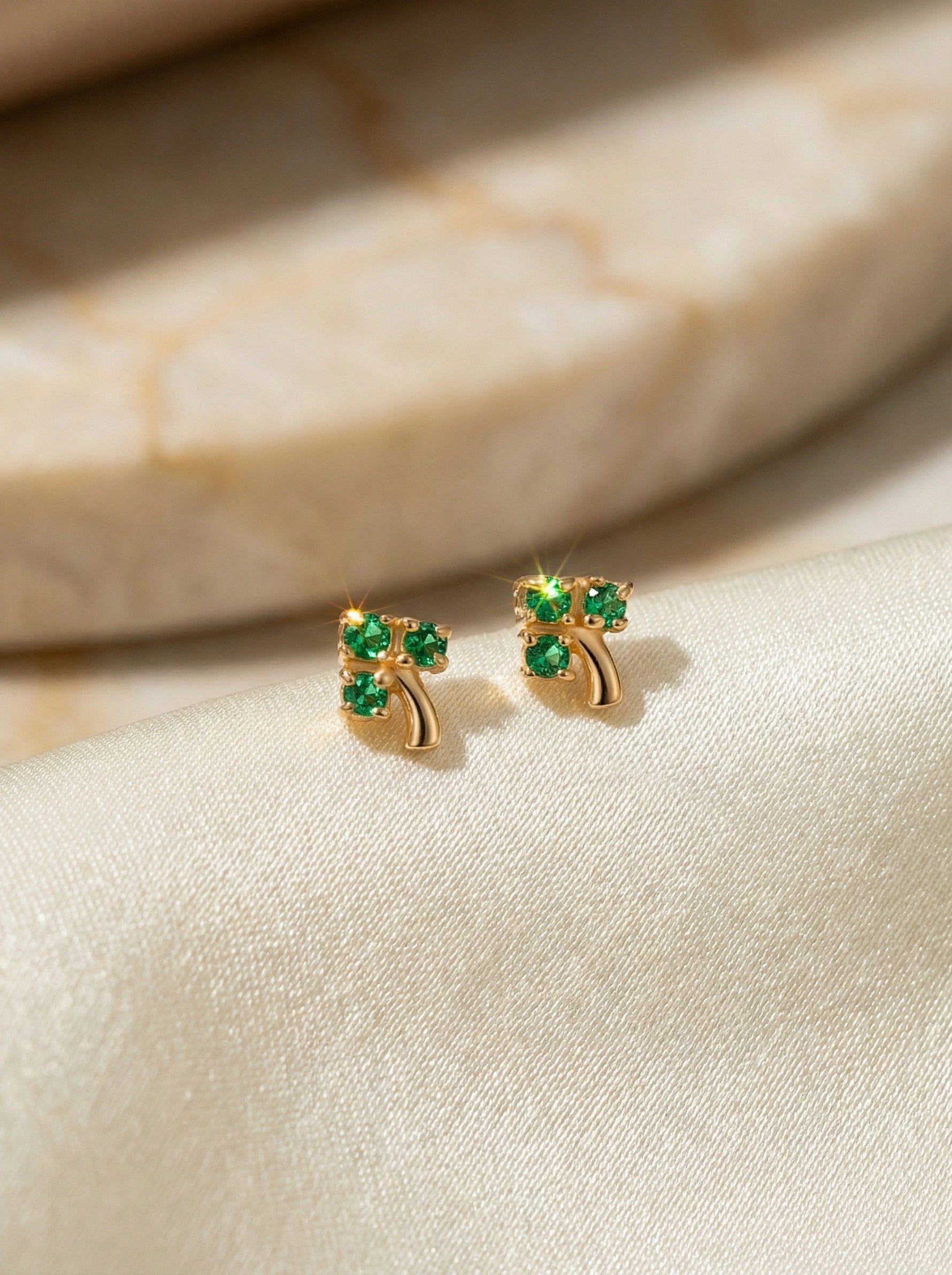 18k Gold plated earrings with green gemstones on a beige fabric background