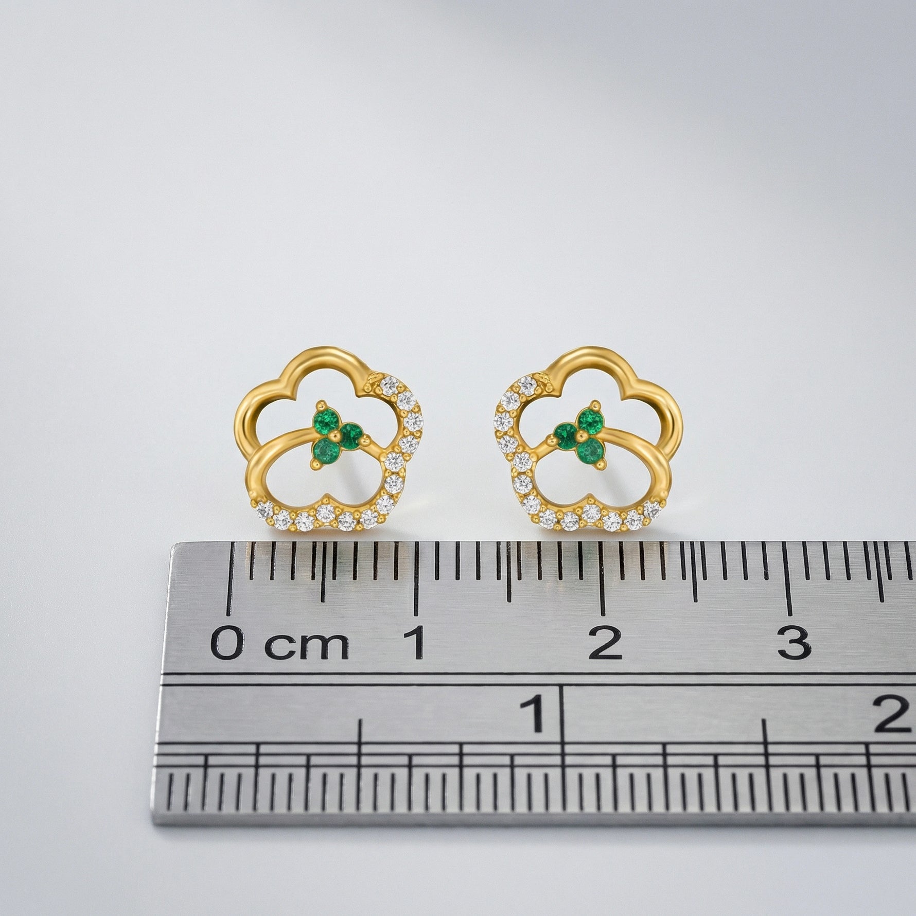 18k Gold plated earrings with green gemstones and clear stones on a ruler for scale.