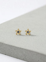 18k Gold plated flower-shaped earrings with blue stones on a gray surface