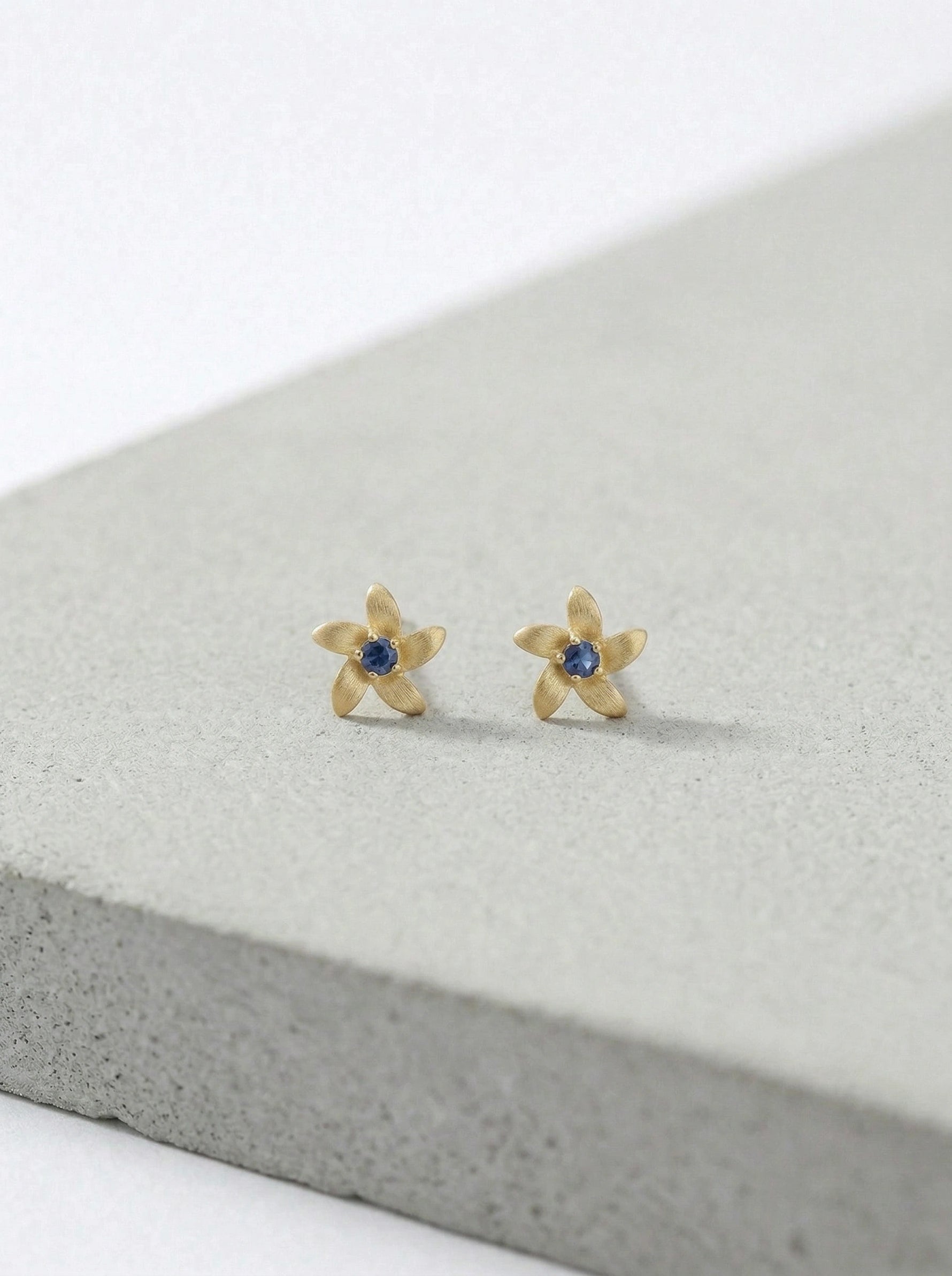 18k Gold plated flower-shaped earrings with blue stones on a gray surface