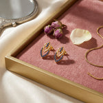 18k Gold plated earrings with blue stones on a pink tray with flowers and a mirror.