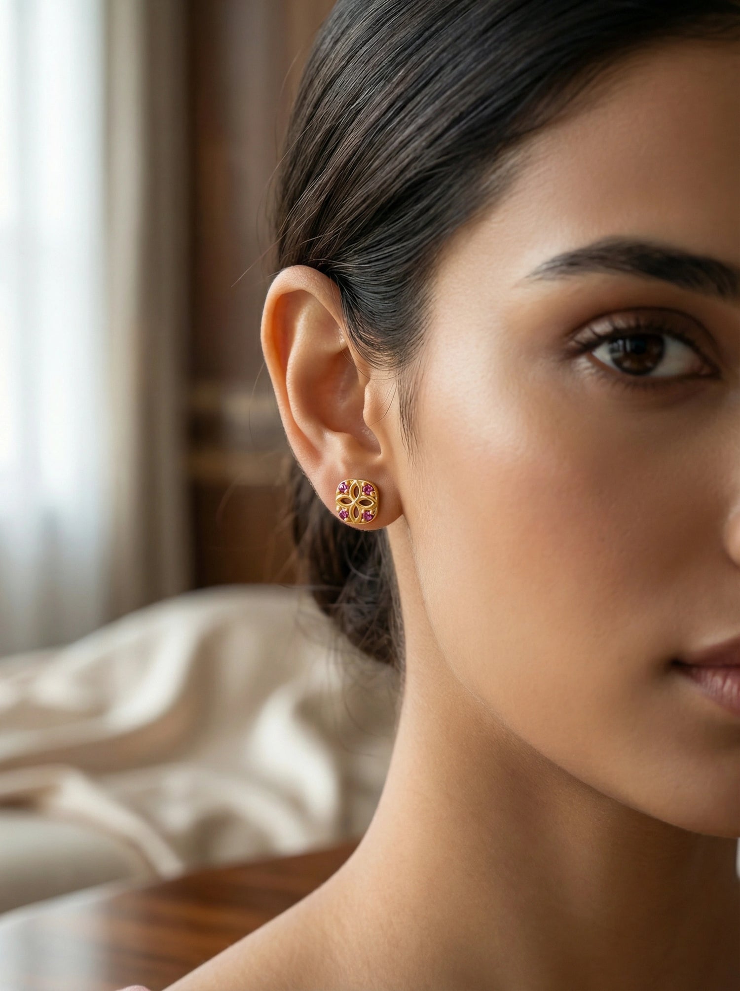 Close-up of a woman wearing 18k gold plated earrings with a blurred background
