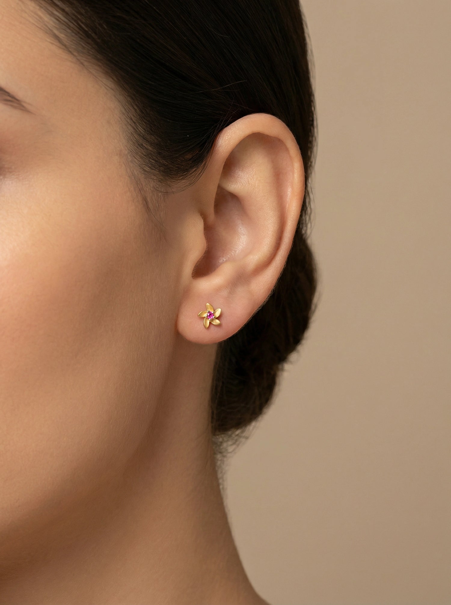 Close-up of an ear wearing a 18k  gold plated floral earring against a beige background