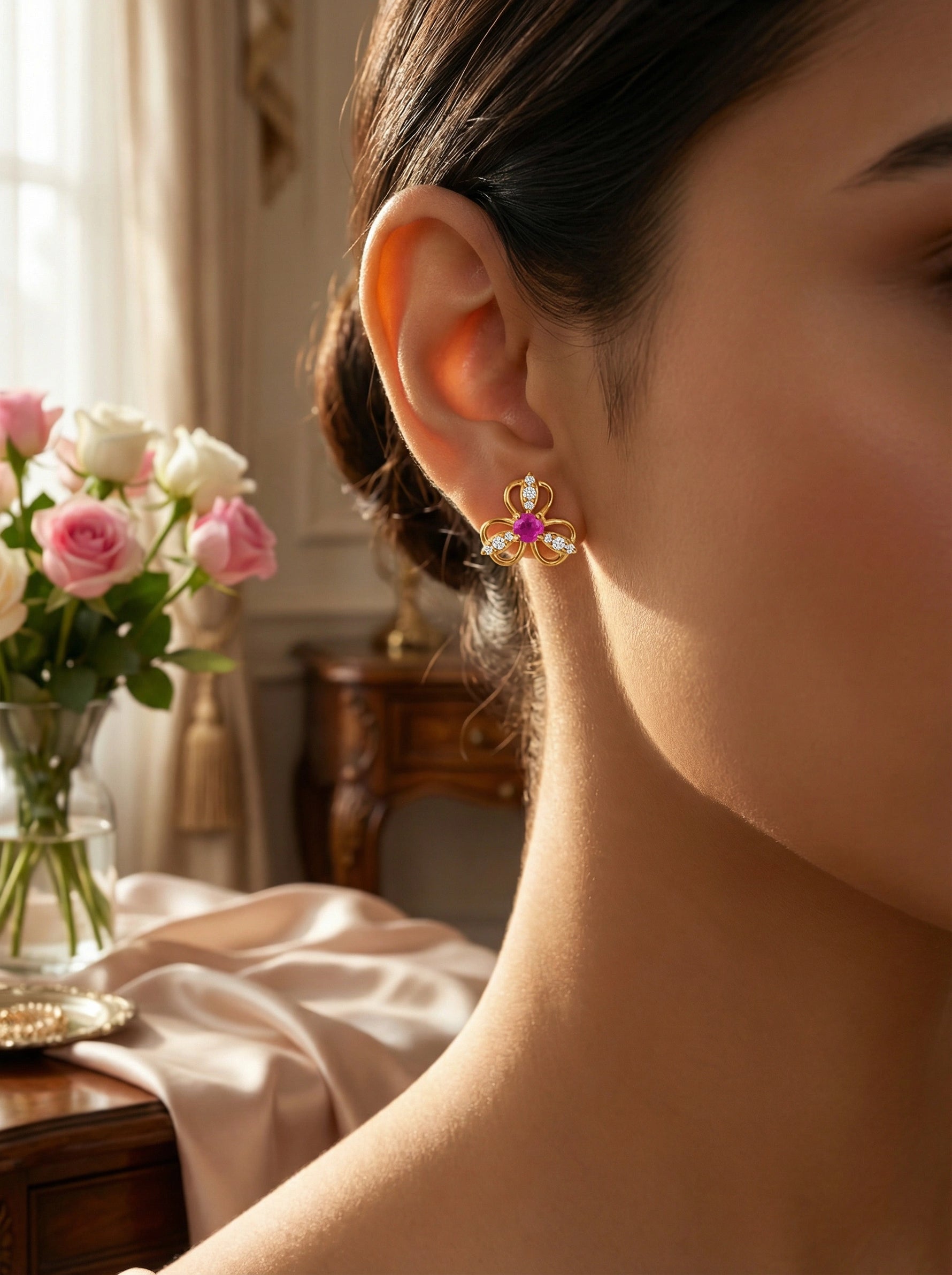 Close-up of a person wearing a 18k gold plated decorative earring with a blurred background of flowers and furniture.