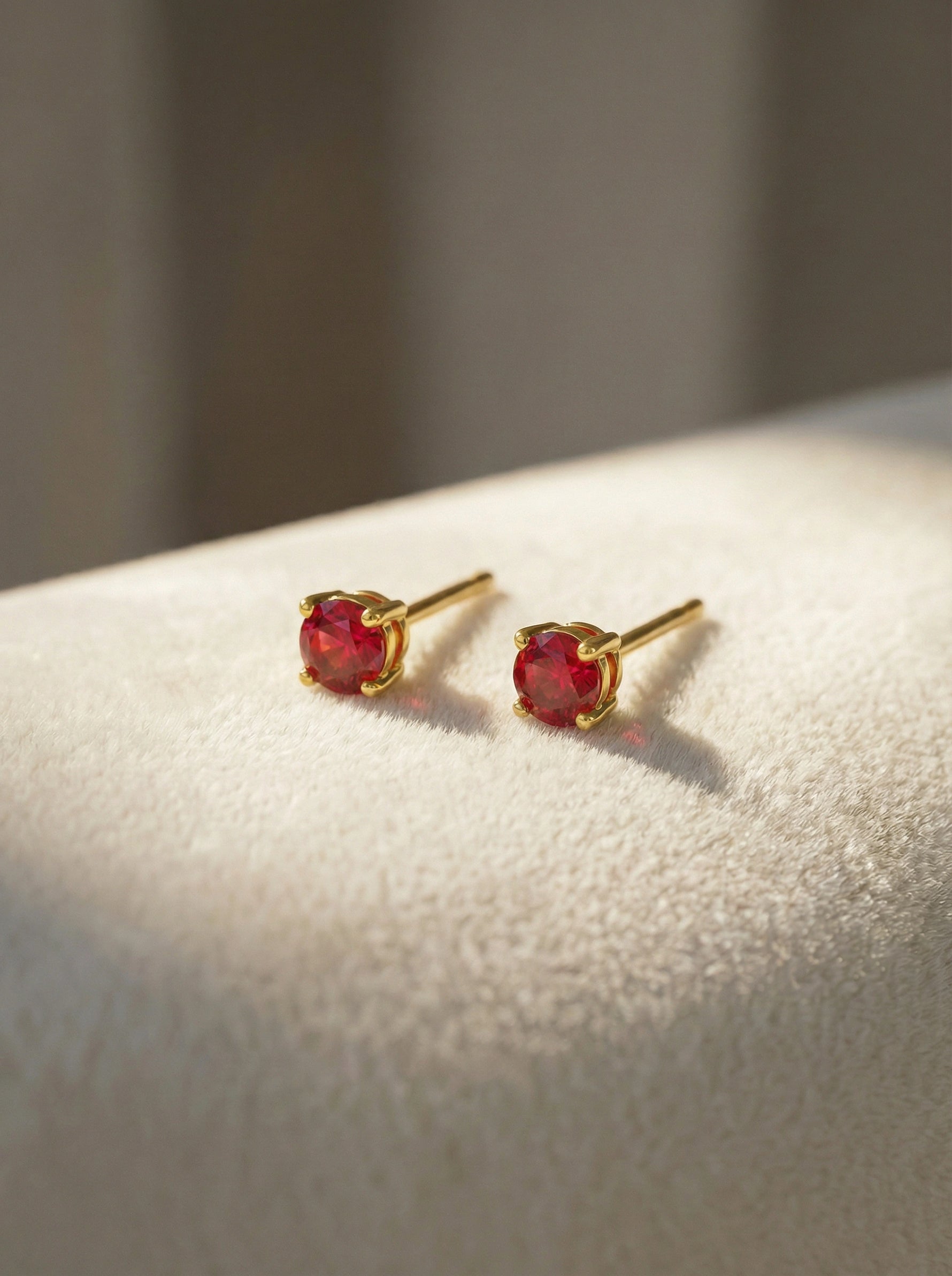 18k Gold plated earrings with red gemstones on a light surface