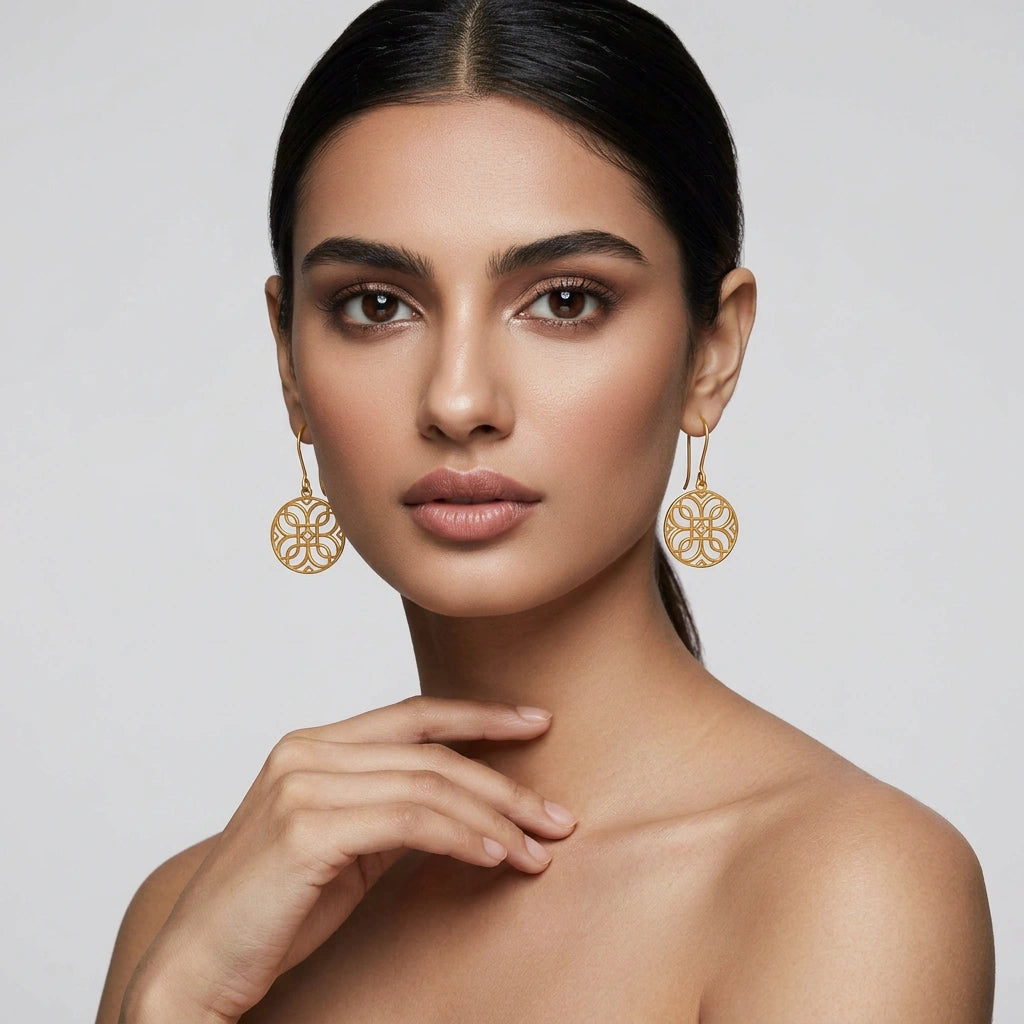 Woman wearing 18k gold plated earrings against a plain background