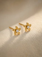  18k Gold plated flower-shaped earrings with diamond centers on a gold background