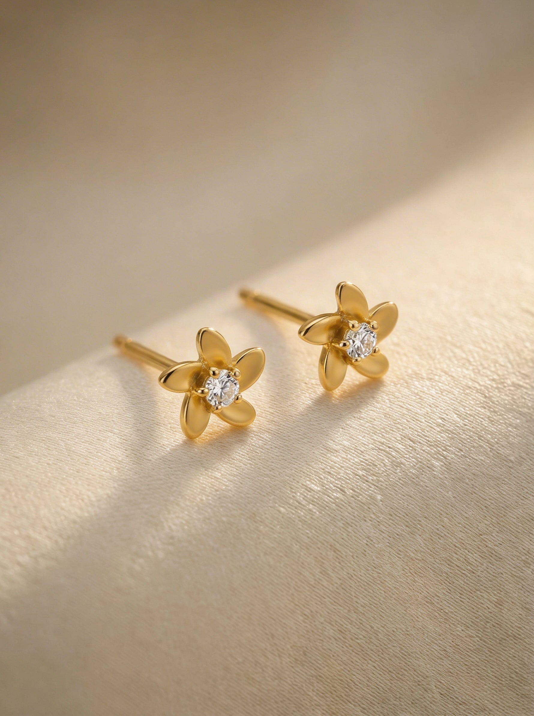  18k Gold plated flower-shaped earrings with diamond centers on a gold background