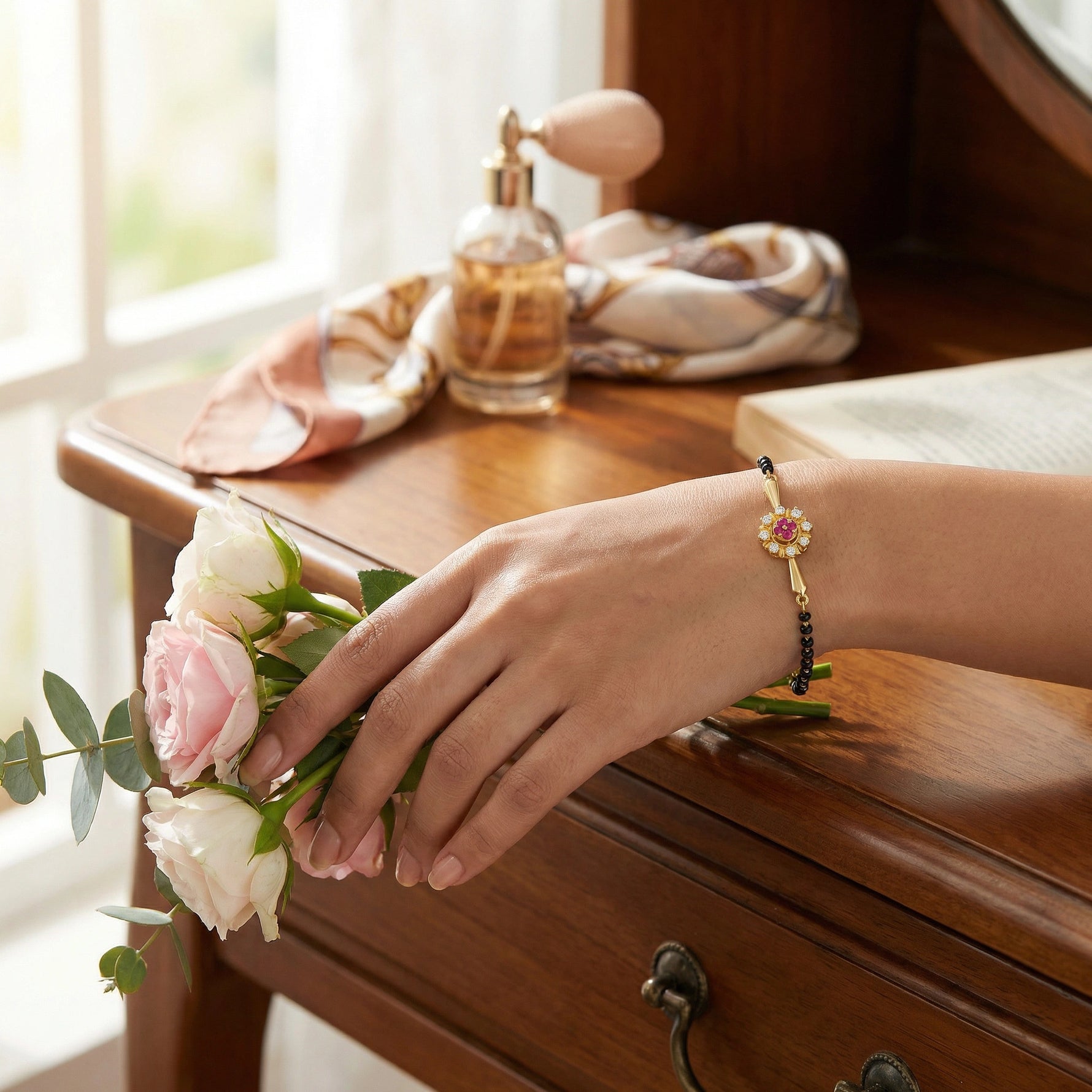 Hand holding flowers with 18k gold plated  bracelet on a wooden surface next to a bottle of perfume.