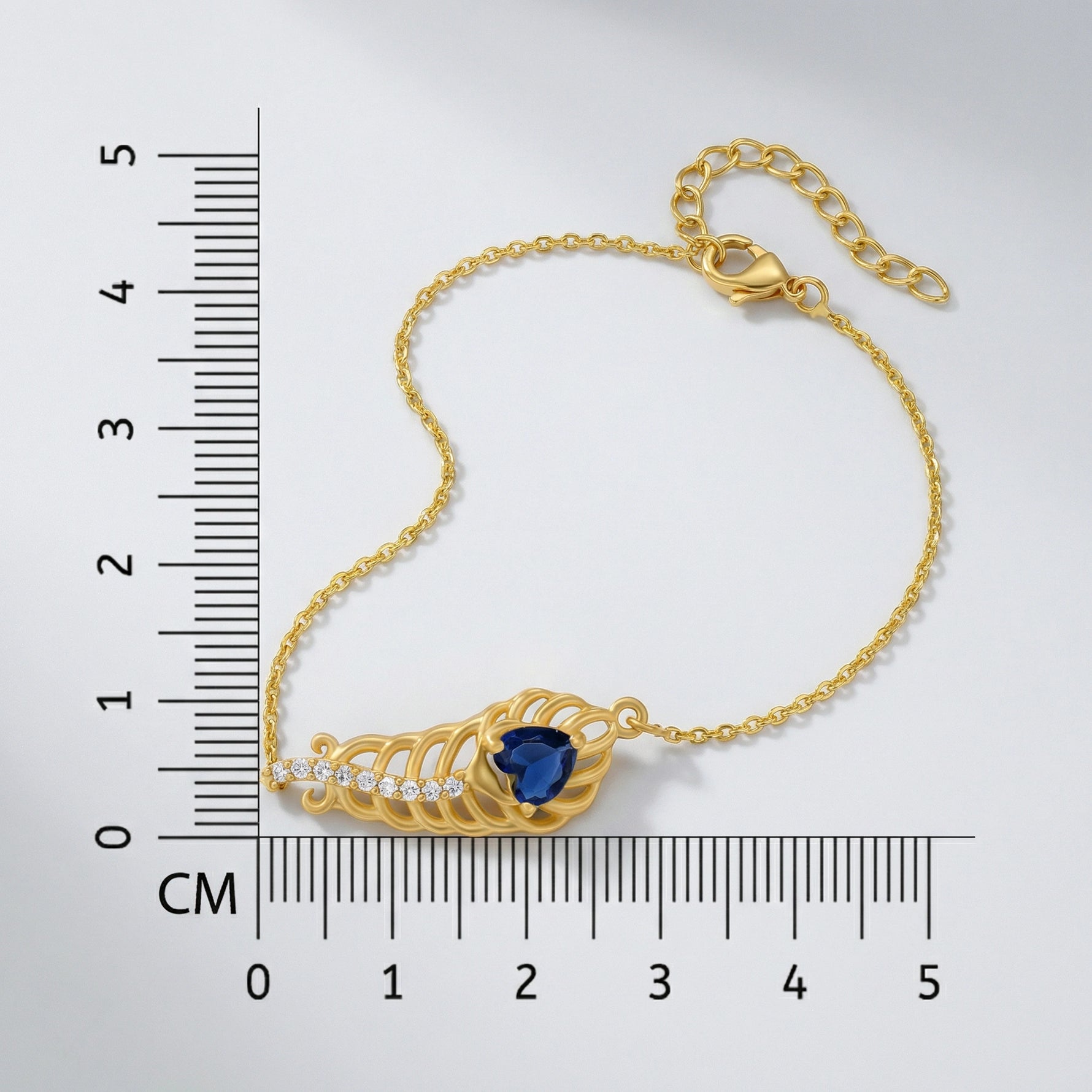 18k Gold plated bracelet with a blue gemstone next to a ruler for measurement on a white background