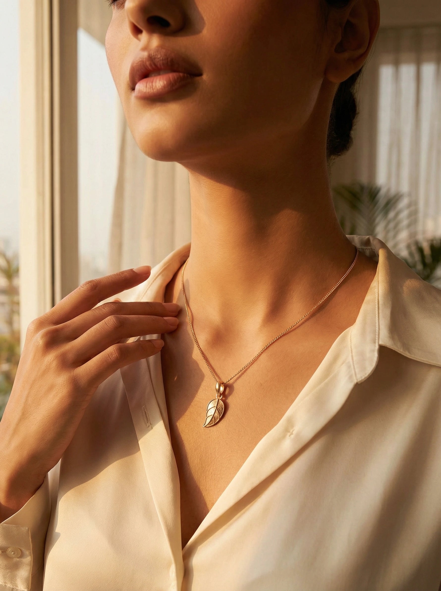 Woman wearing a 18K gold PLATED necklace with a leaf pendant in a bright indoor setting