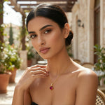 Woman wearing a 18k gold plated necklace with a red gemstone in an outdoor setting