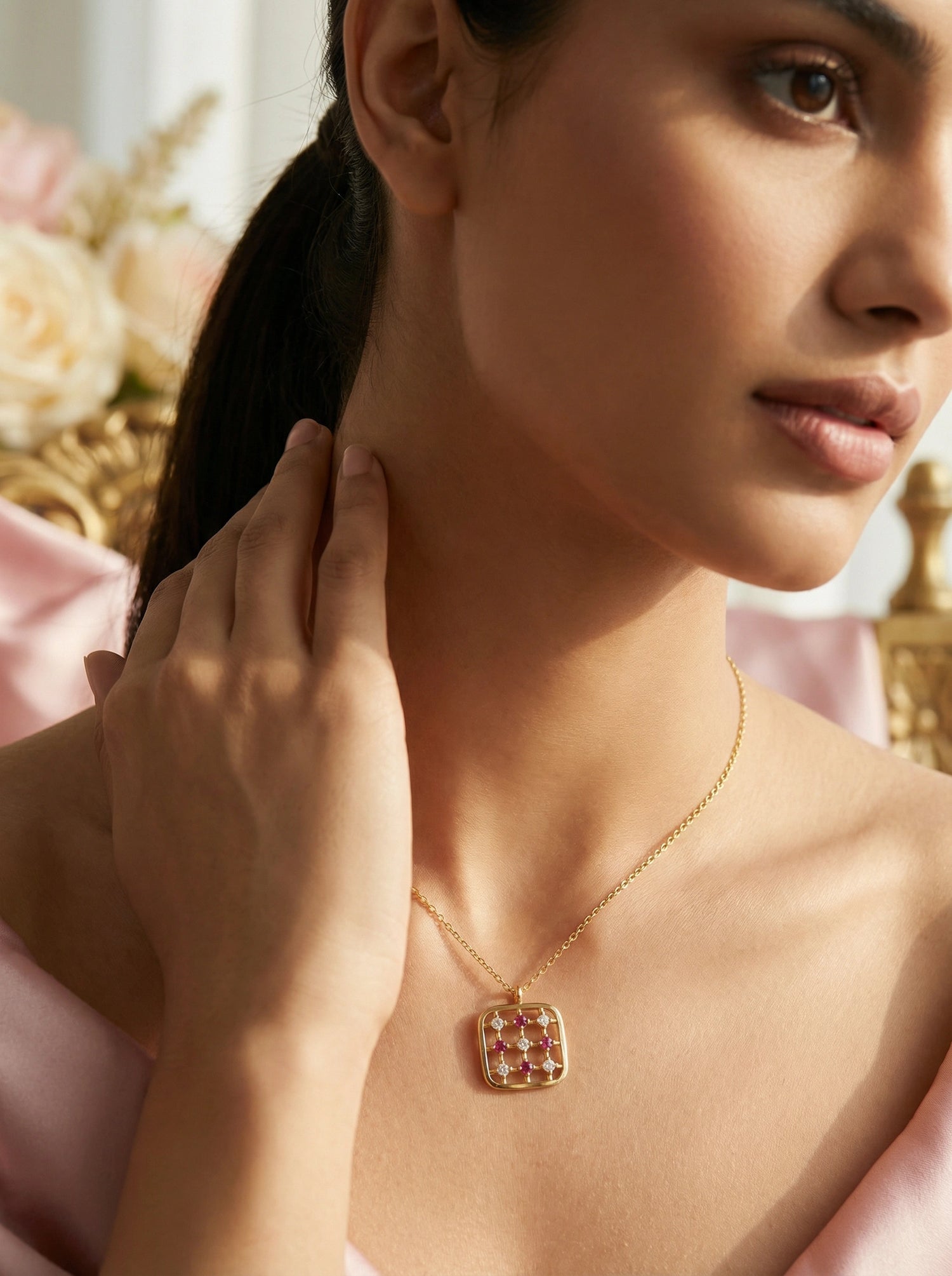 Woman wearing a 18k gold plated necklace with a red gemstone pendant, touching her neck.