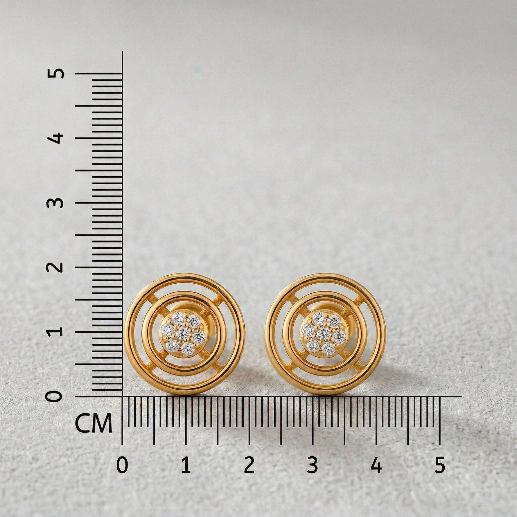 18k Gold plated earrings with diamond accents next to a ruler on a light gray background