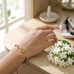 Hand wearing 18k  gold plated bracelet with a small bouquet of white flowers on a wooden surface.