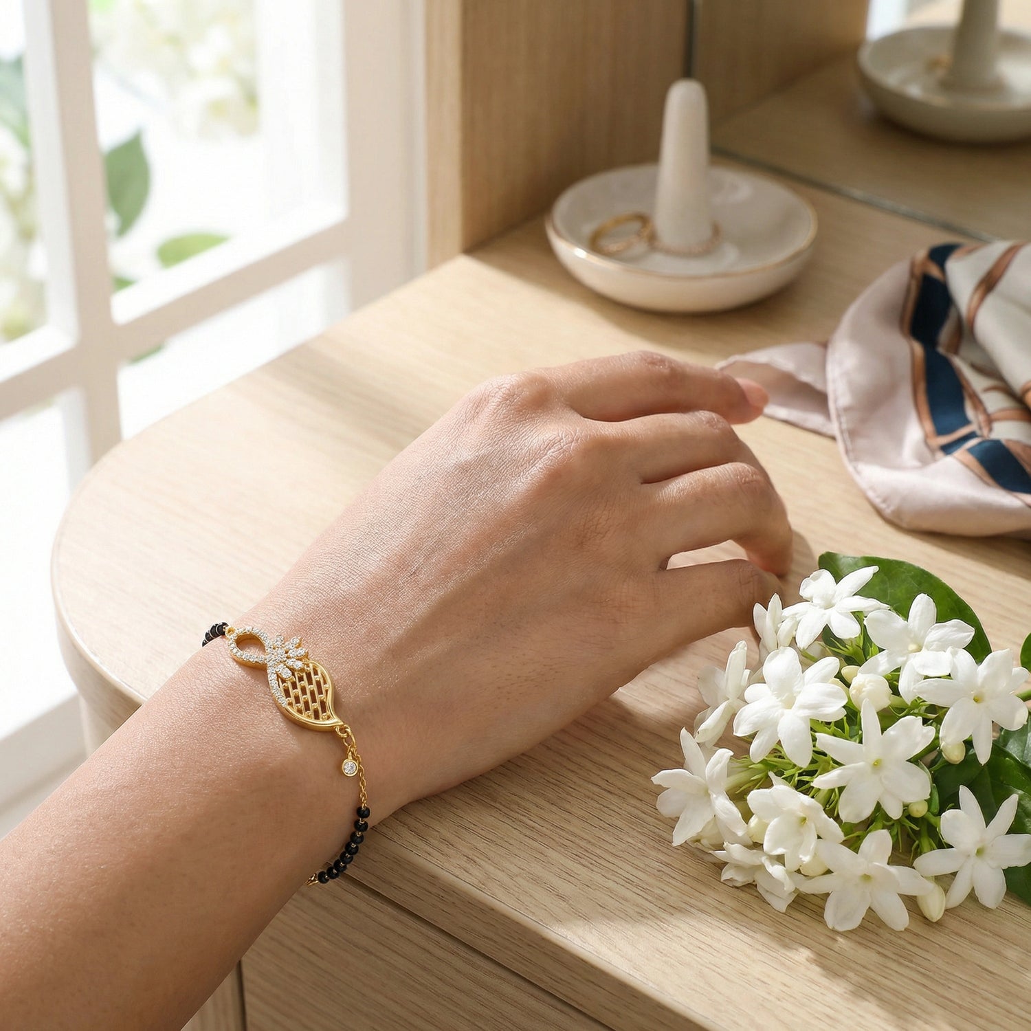 Hand wearing 18k  gold plated bracelet with a small bouquet of white flowers on a wooden surface.