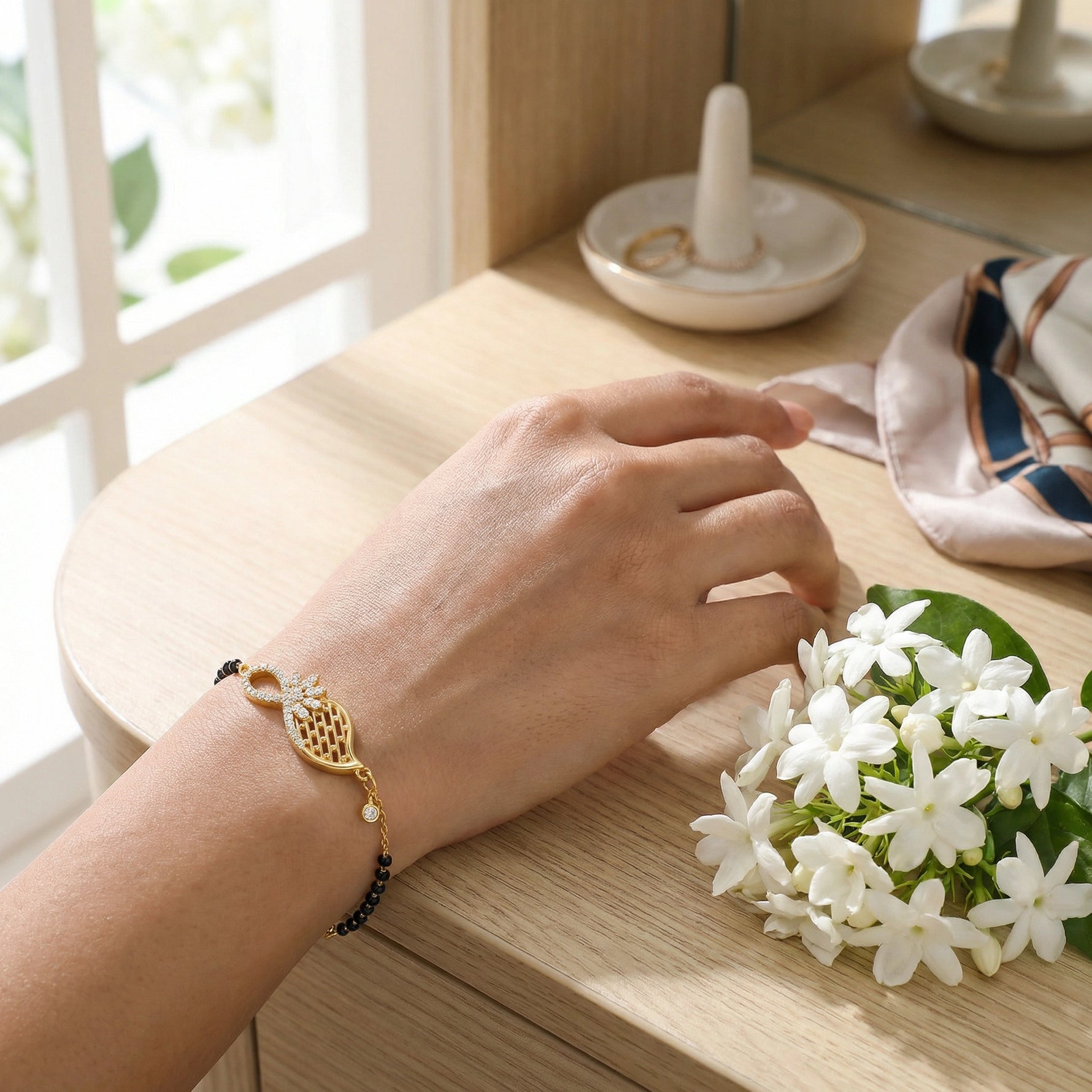 Hand wearing 18k  gold plated bracelet with a small bouquet of white flowers on a wooden surface.