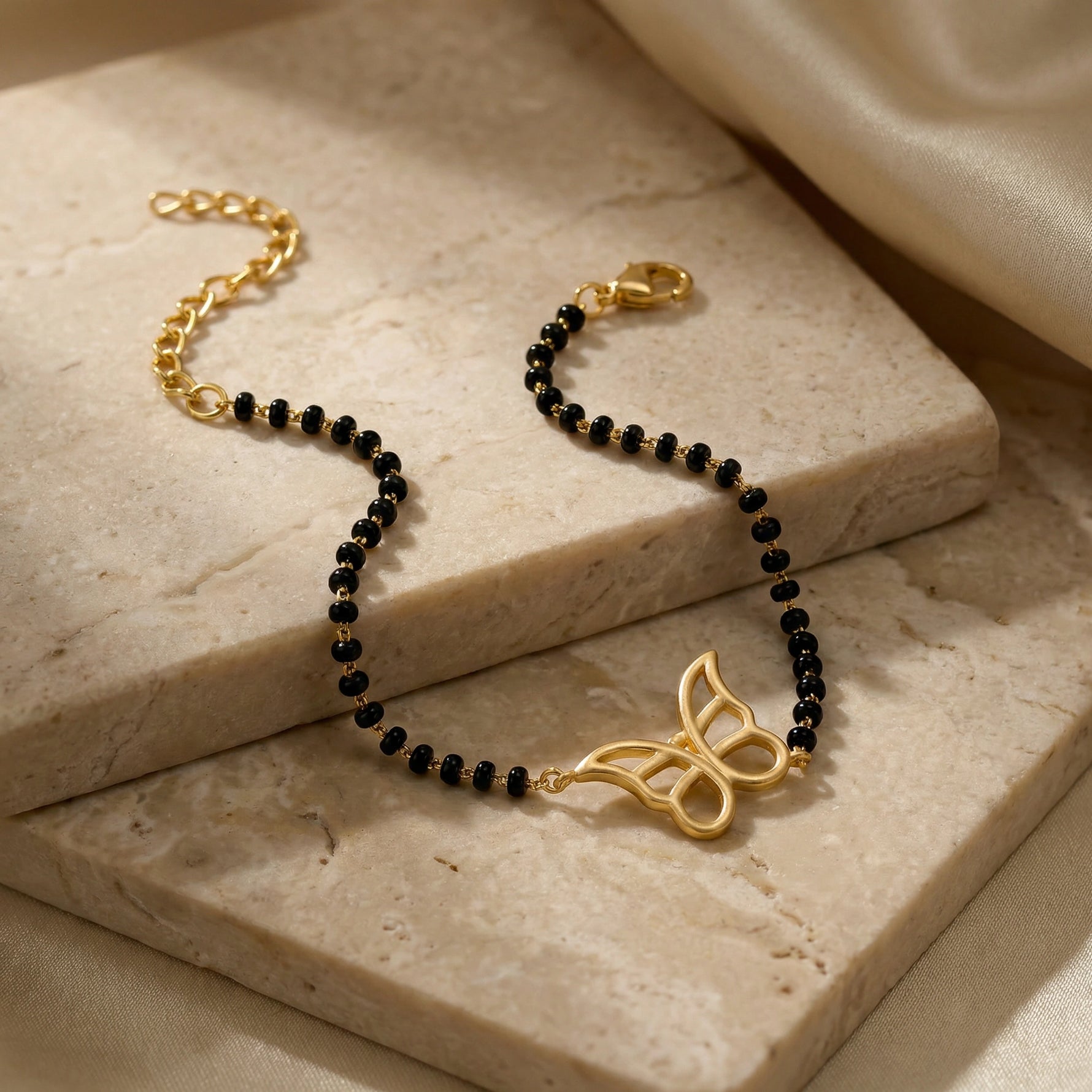 Black beaded bracelet with 18k gold plated clasp and decorative element on a marble surface