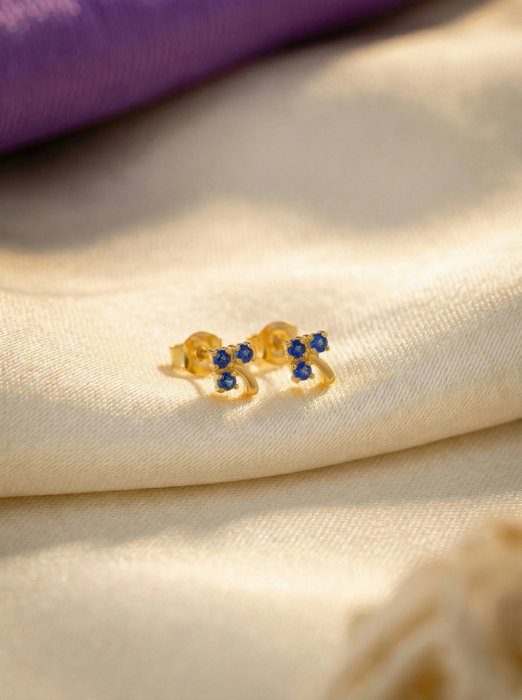 18k Gold plated  bow-shaped earring with blue stones on a beige fabric background