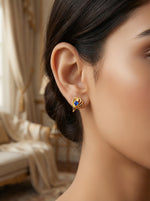 Close-up of a woman wearing a 18k gold plated earring with a blue gemstone, blurred background