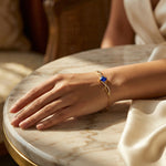 Hand wearing a 18k gold plated  bracelet with a blue stone on a marble surface