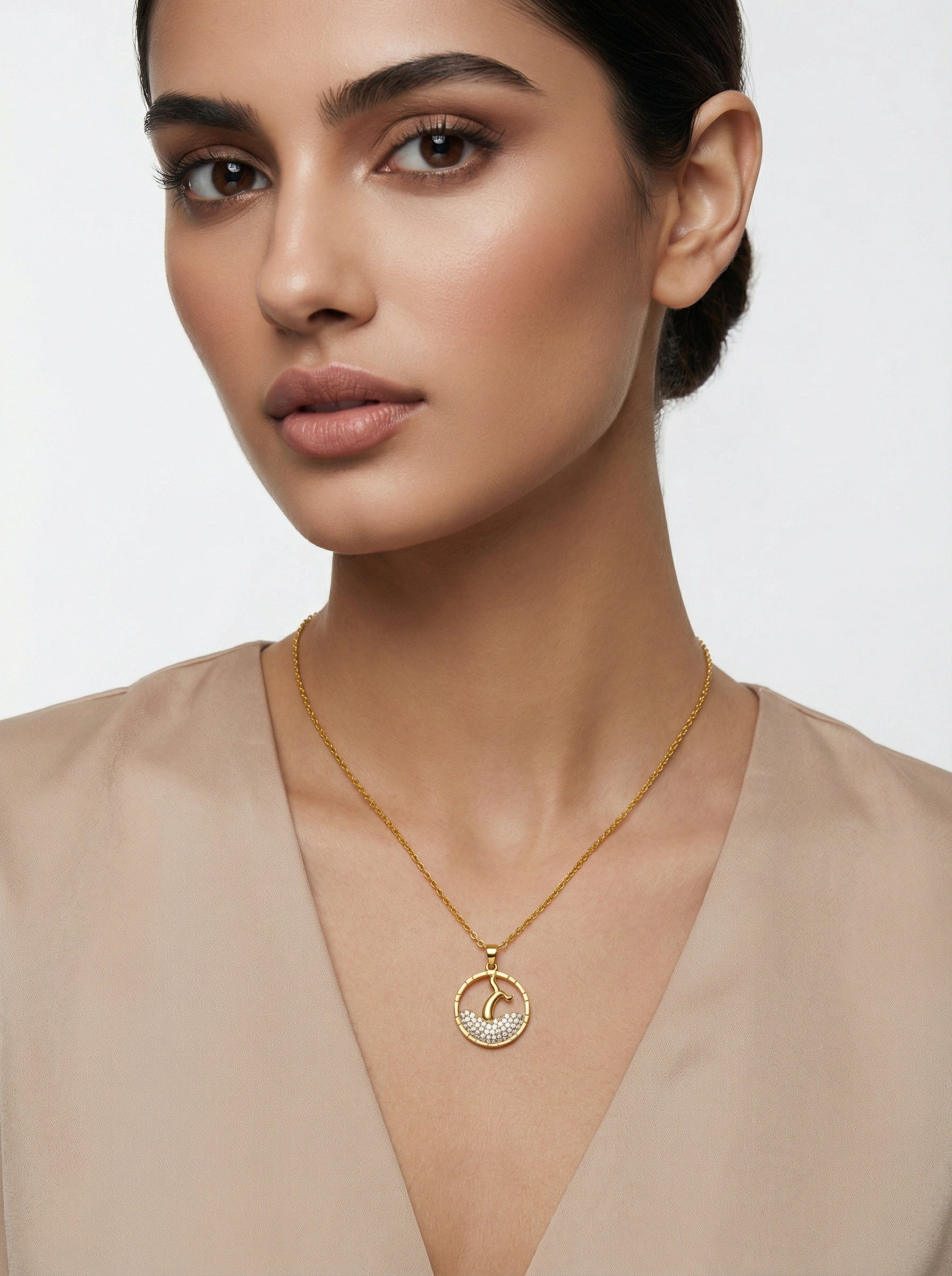 Woman wearing a 18k gold plated necklace with a circular pendant on a plain background