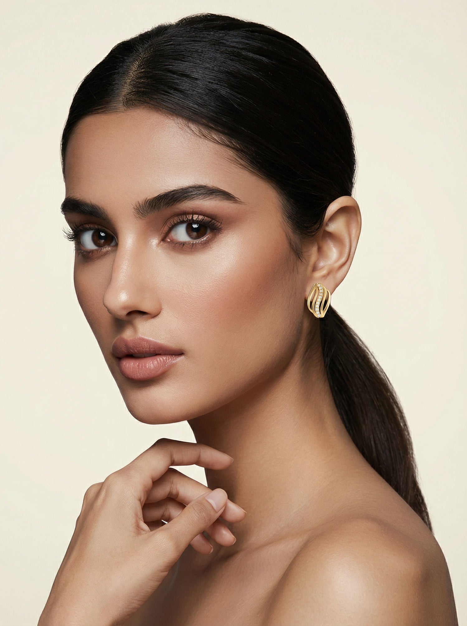 Woman with a ponytail wearing 18k gold plated earrings against a beige background