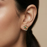 Close-up of an ear wearing a 18k gold plated earring with a green gemstone on a beige background