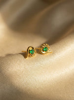 18k Gold plated earrings with green gemstones on a beige fabric background