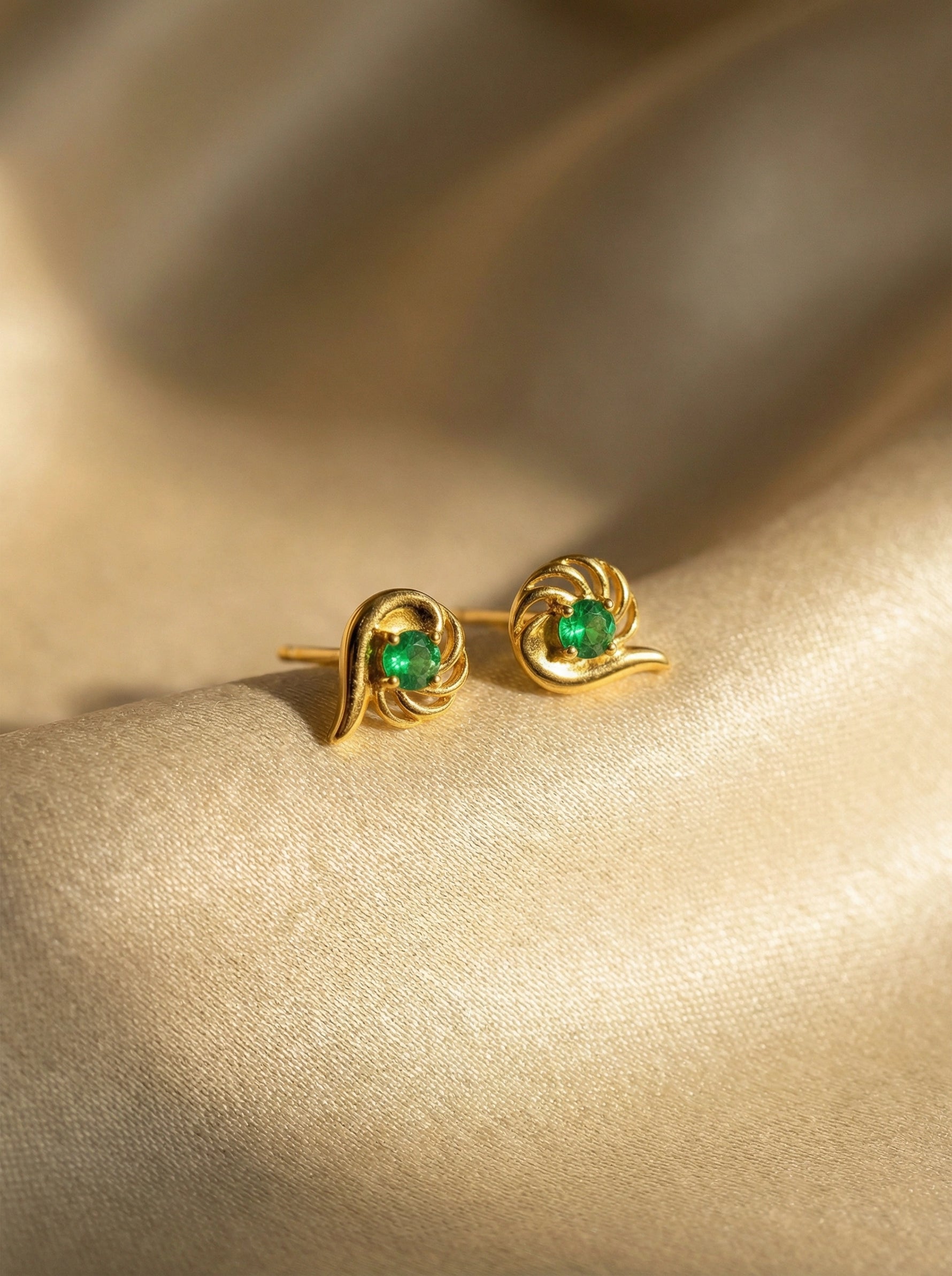 18k Gold plated earrings with green gemstones on a beige fabric background
