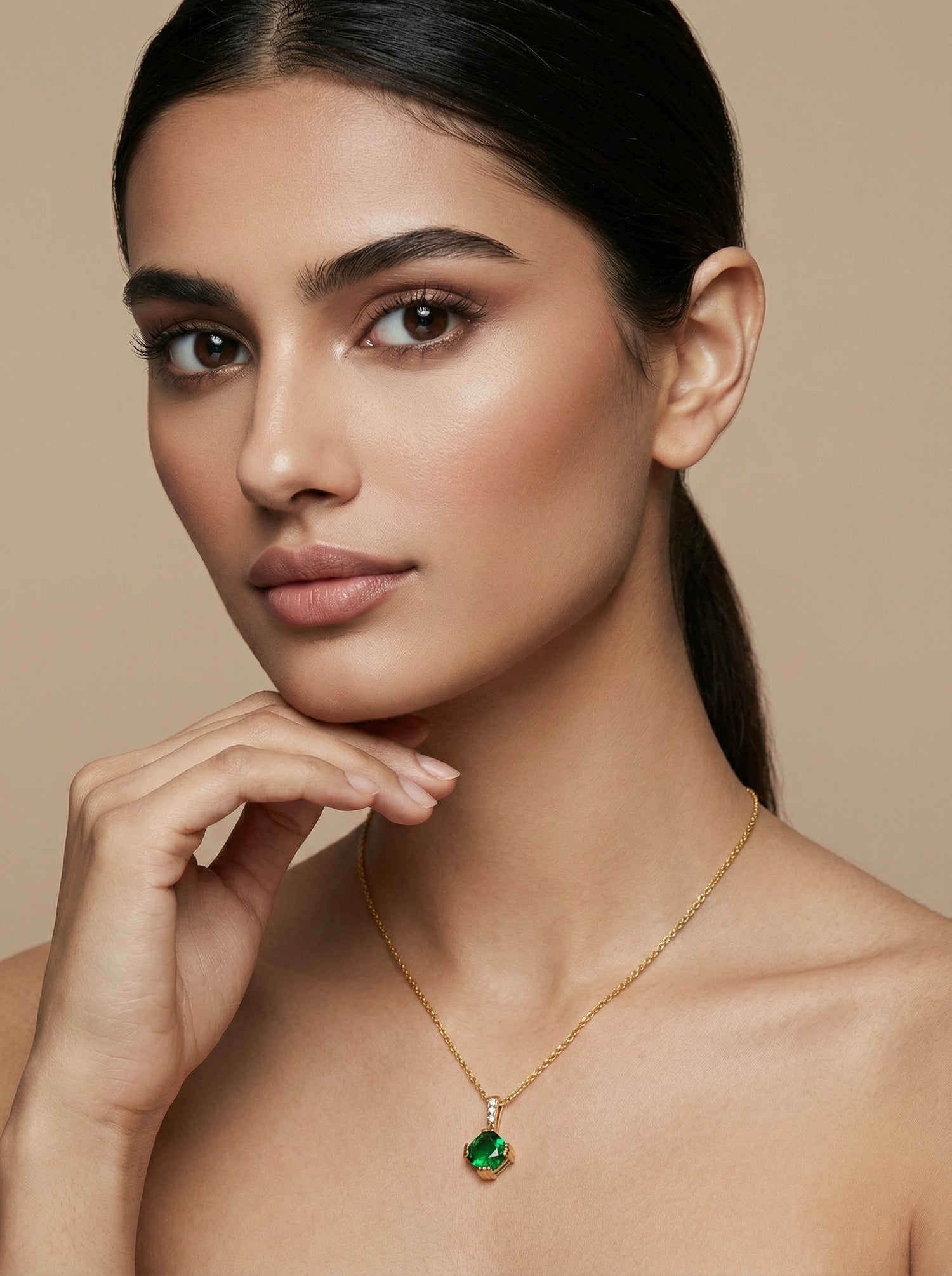 Woman wearing a 18k gold plated necklace with a green pendant against a beige background