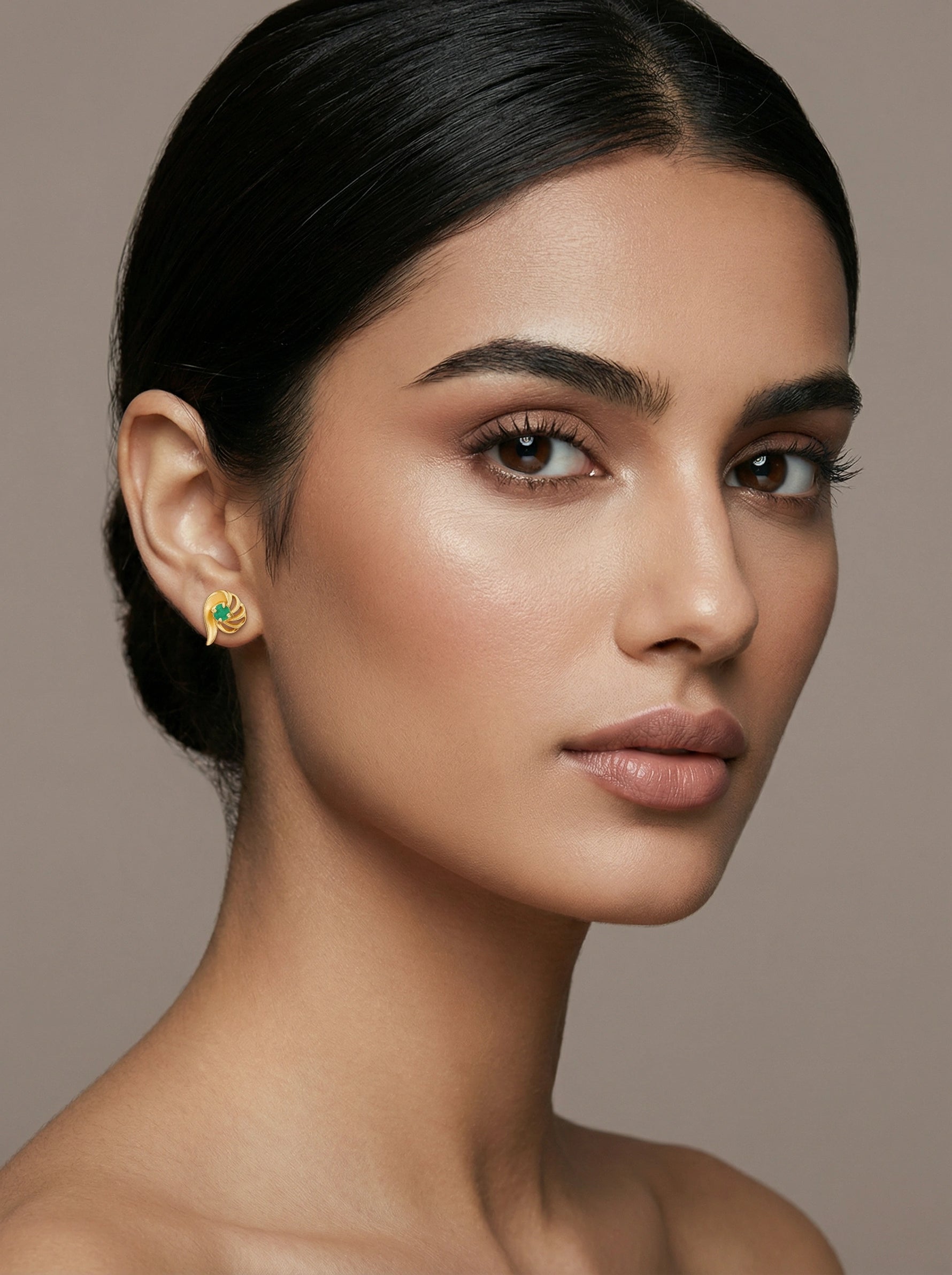 Close-up of a woman wearing a 18k  gold plated earring with a green gemstone on a neutral background