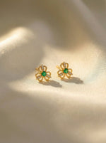 18k Gold plated flower-shaped earrings with green gemstones on a beige background