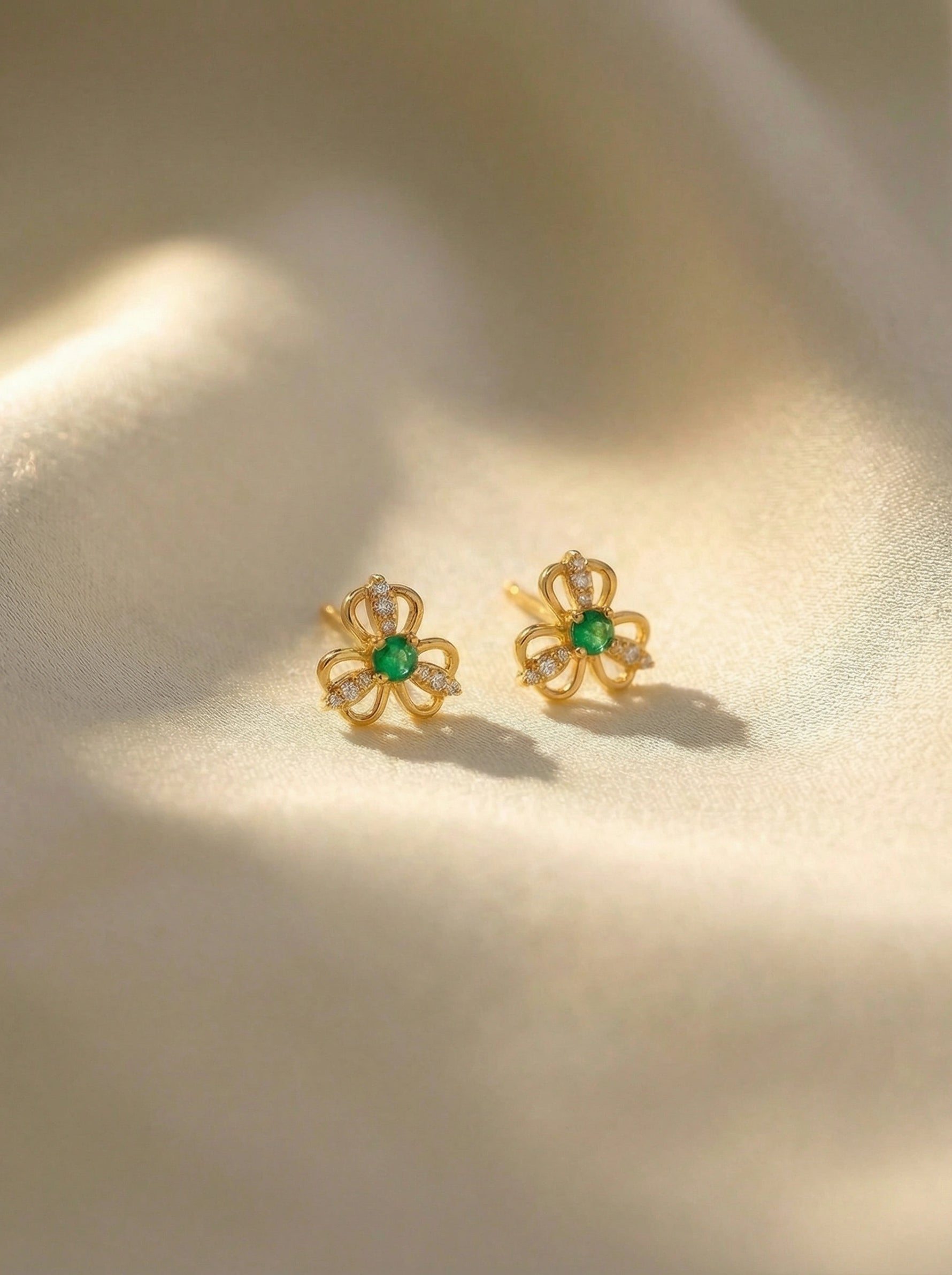 18k Gold plated flower-shaped earrings with green gemstones on a beige background