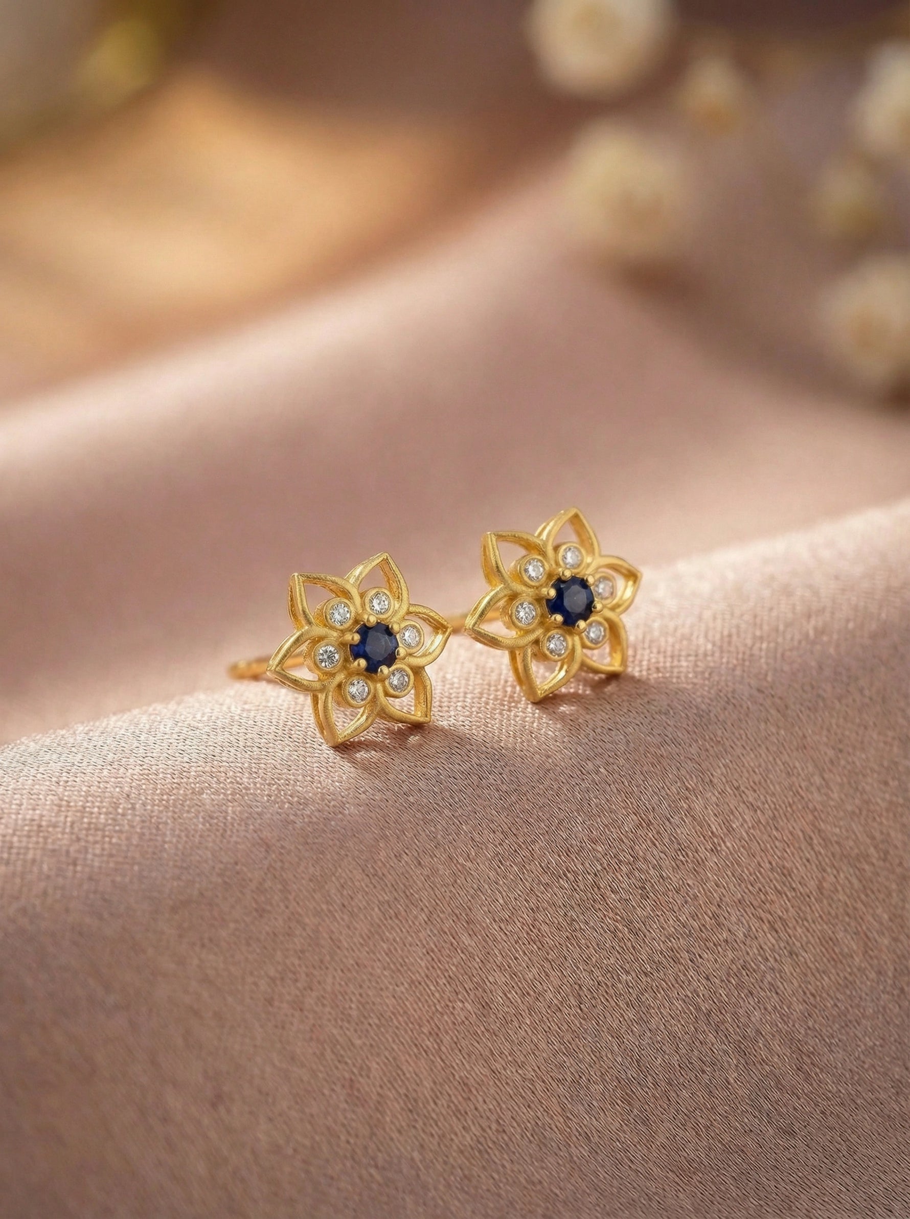  18k Gold plated  flower-shaped earrings with blue centers on a soft fabric background
