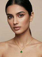Woman wearing a 18k  gold plated necklace with a green pendant against a beige background