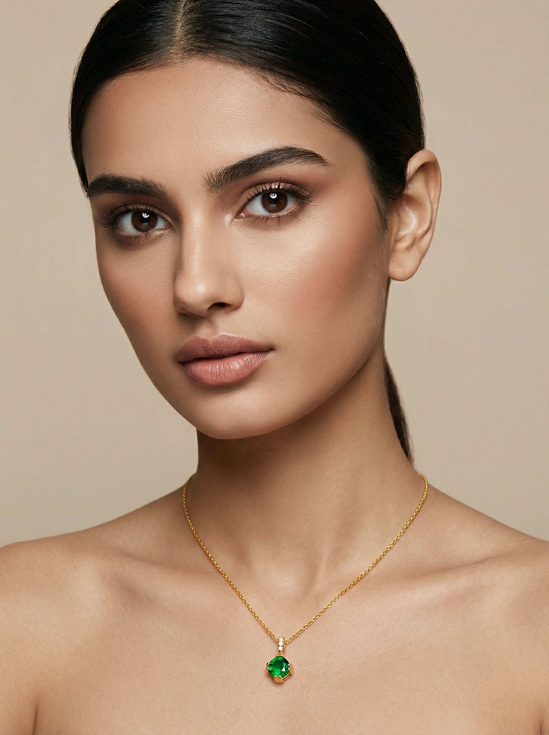 Woman wearing a 18k  gold plated necklace with a green pendant against a beige background